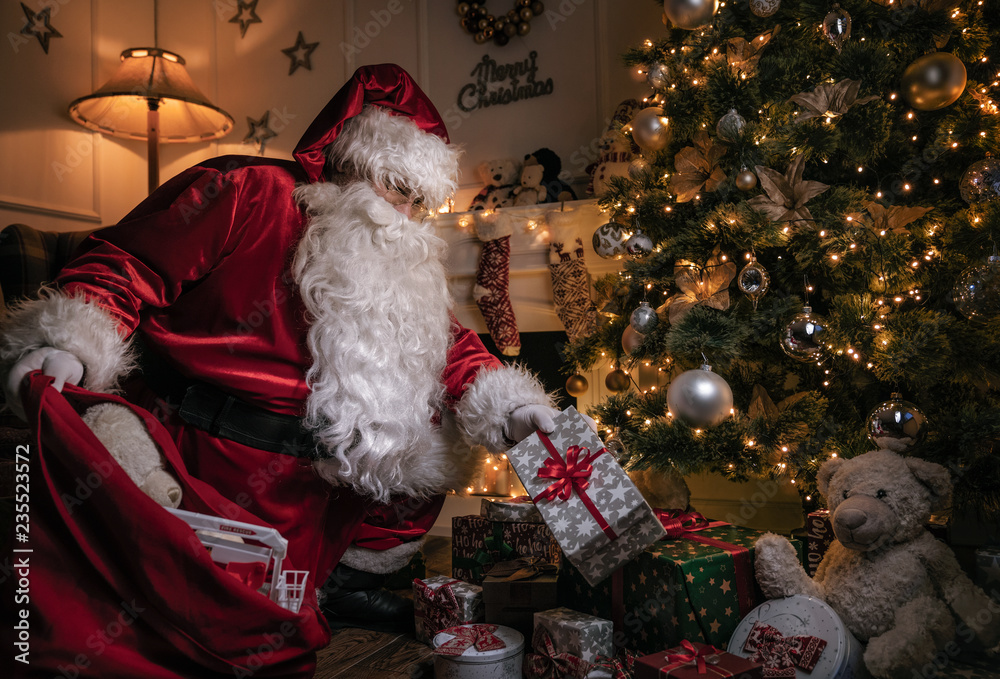 Wall mural Santa Claus putting gifts under the christmas tree