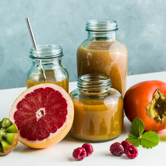 different glasses with freshly made grapefruit, kiwi, persimmon and raspberry smoothies. on white table and blue background. healthy food. morning breakfast