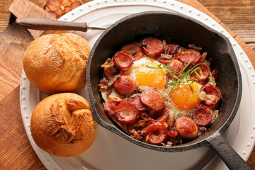 Cooked egg and sausages on rying pan, tasty english breakfast on wooden background