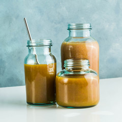 different glasses with freshly made grapefruit, kiwi, persimmon and raspberry smoothies. on white table and blue background. healthy food. morning breakfast