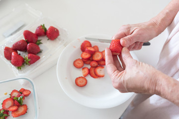 HIgh angle close up view of older woman's hands cutting strawberries (selective focus)
