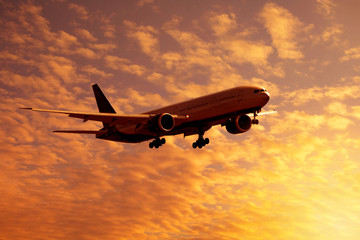Fototapeta na wymiar Dramatic view of a dark silhouette of aircraft against a orange clouds in the sunset sky