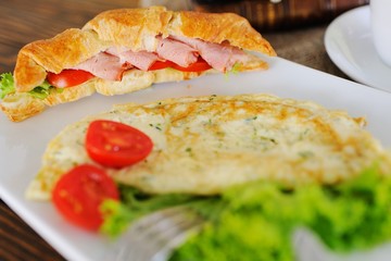breakfast - croissant with ham and tomato on a background of omelette and green salad on a wooden background close-up