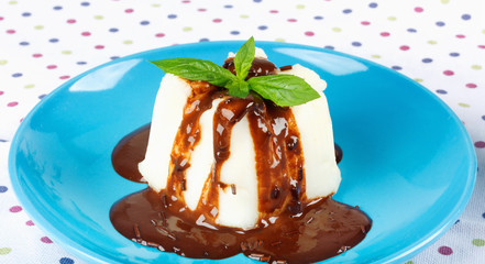 Cream pudding with chocolate sauce and mint on  multicolored tablecloth.