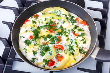 Traditional rustic omelette with bacon, pasta and greens on  old black frying pan on background of vintage  table.