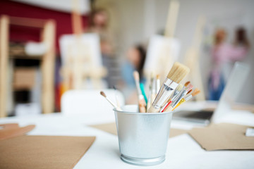 Small bucket with bunch of paintbrushes and papers on workplace of artist in studio