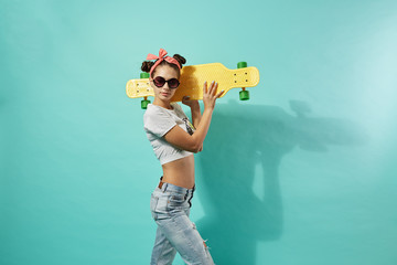 Funny young girl in sunglasses and pink bow on her head dressed in jeans and top stands with yellow...