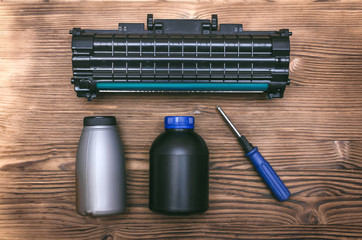 Laser printer cartridge, screwdriver and bottles with toner on the table. Office equipment...