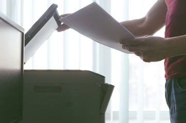 Businessman is holding in hands a heap of documents and is working with printer or scanner. Office paperwork concept.