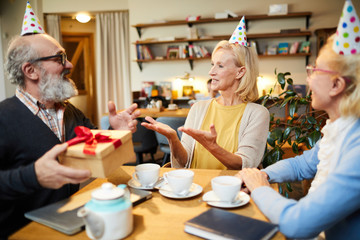 Three happy senior people in birthday caps having celebration in cafe at tea party