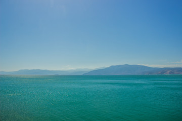 abstract wallpaper landscape of mountain ridge horizon silhouette and sea calm water surface in clear morning foggy weather time, copy space 