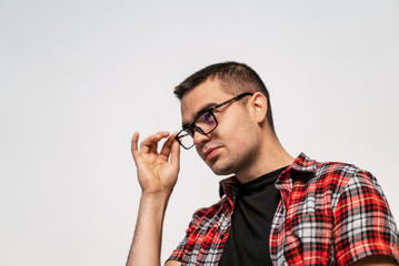 Handsome guy in eyeglasses and white t-shirt over the white studio background. Smart man touching his glasses in black frame and looking ahead.