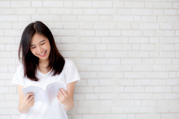 Beautiful of portrait young asian woman happiness relax standing reading book on concrete cement white background at home, girl happy study content literature, education and lifestyle concept.