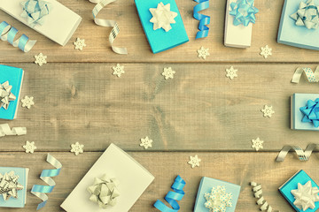 Small blue and white boxes with bows, ribbons and snowflakes, arranged in a circle. Christmas composition with copy space on wooden background. Festive layout.