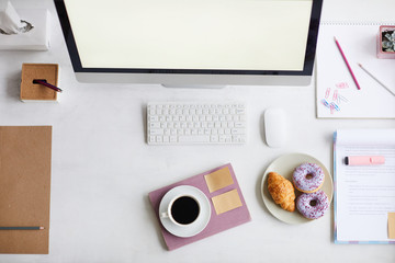 Computer monitor, pastry, cup of coffee, notepad with crayons and business document with pink...