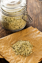 Heap of raw, organic hemp seeds on brown paper with hemp seeds in storage jar on rustic table