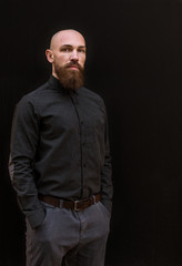 bald man with a beard in a black shirt on a dark background