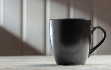 Ceramic Black mug with patterns on a white wooden table, in the morning sun rays