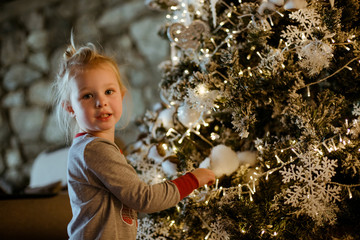 A charming white girl looks at the decorated Christmas tree and the lights on it. Family friendly Christmas concept.