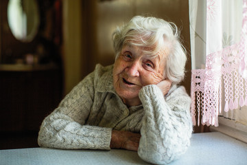 Portrait of elderly pensioner lady sitting at the table. - obrazy, fototapety, plakaty