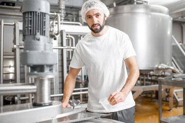 Portrait of a handsome worker in uniform near the stainless tank full with fermenting milk at the cheese manufacturing