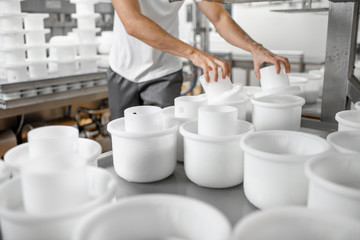 Man in uniform forming cheese into the plastic molds putting them under the press at the cheese...