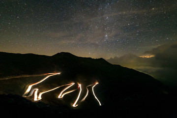 Car driving down the mountain pass road under a starry sky, Stelvio, italian alps. Composite of...