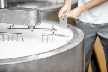 Man mixing milk in the stainless tank during the fermentation process at the cheese manufacturing. Close-up view with no face
