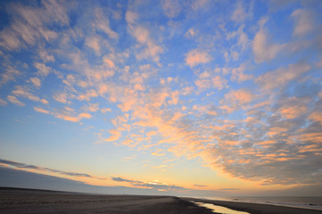 Fototapeta na wymiar Zachód Słońca na plaży pod częściowo zachmurzonym niebem.