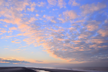 Fototapeta na wymiar Zachód Słońca na plaży pod częściowo zachmurzonym niebem.