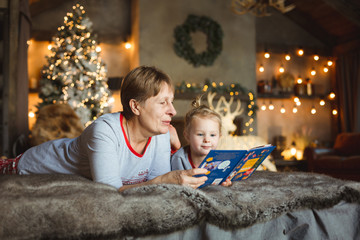 Grandma and granddaughter have fun together reading a book on the bed . Family Christmas concept.