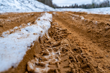 Car Tire Marks on an Empty Field Covered With Snow, Wood in the Background - Cloudy Day