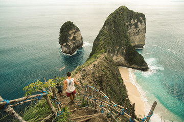  Adventurous man standing on top of Kelingking beach and unique rock formations on Nusa Penida,...