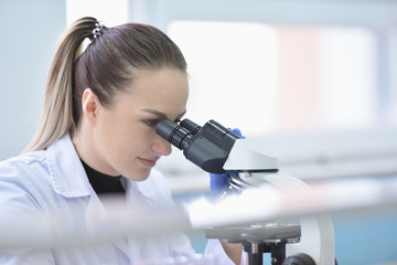 Young female male scientist looking through a microscope in a laboratory doing research, microbiological analysis, medicine.