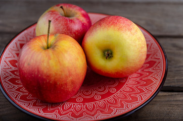 Naklejka na ściany i meble Apples in a ceramic red plate on a wooden table.
