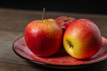 Apples in a ceramic red plate on a wooden table.