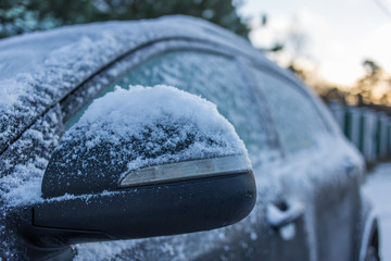 Car's side view mirror of a modern car covered  with snow