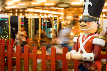 Tin soldier in an amusement park with a carousel moving in the background