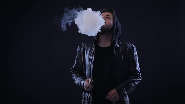 Man smoking electronic cigarette, vape in dark clothes. vapor on black isolated background.