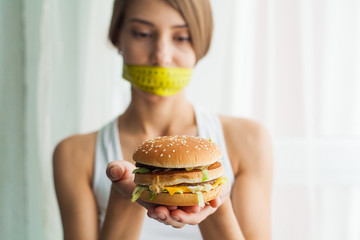 Diet concept and health. Emotional woman with measuring tapes around her mouth and unhealthy foodat...