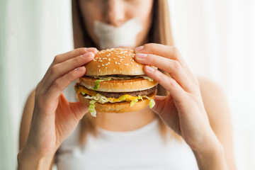 Diet. Young woman with duct tape over her mouth, preventing her to eat junk food. Healthy eating concept