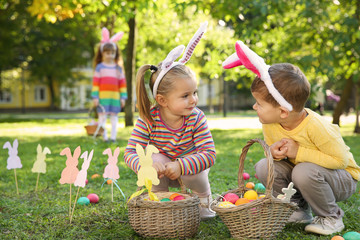 Naklejka premium Cute little children hunting eggs in park. Easter tradition