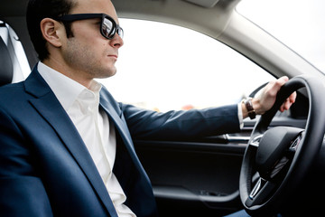 man in suit sits behind the wheel of a car