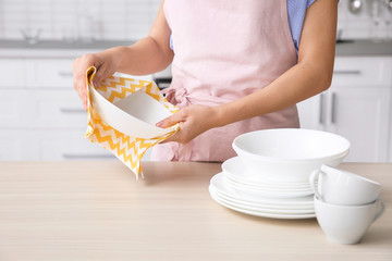 Woman wiping clean dish at table in kitchen, closeup