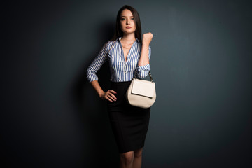 Woman in office clothes with a little white bag on a dark background