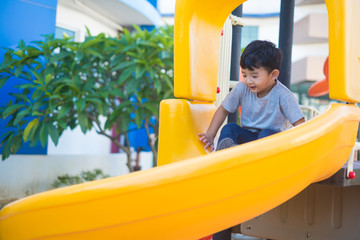 Asian kid playing slide at the playground under the sunlight in summer, Happy kid in kindergarten or preschool school yard.