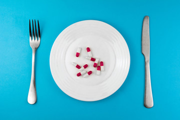 pharmaceutical medicine pills or capsules on a plate with a fork and knife. top view blue background.  prescription weight loss drugs concept