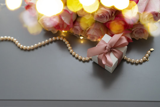 Fototapeta Rose fresh flowers bouquet with gift box on gray table from above, flat lay scene with bokeh lights