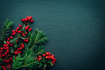 Frame with fir branches and Pyracantha decorations on dark stone background. Top view.