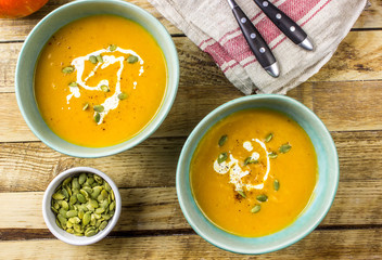 Roasted pumpkin and carrot soup with cream and pumpkin seeds on wooden background. Top view. Copy space